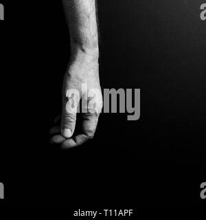 Black & white image of man`s hand hanging loosely, isolated against a black background with dramatic sidelight Stock Photo